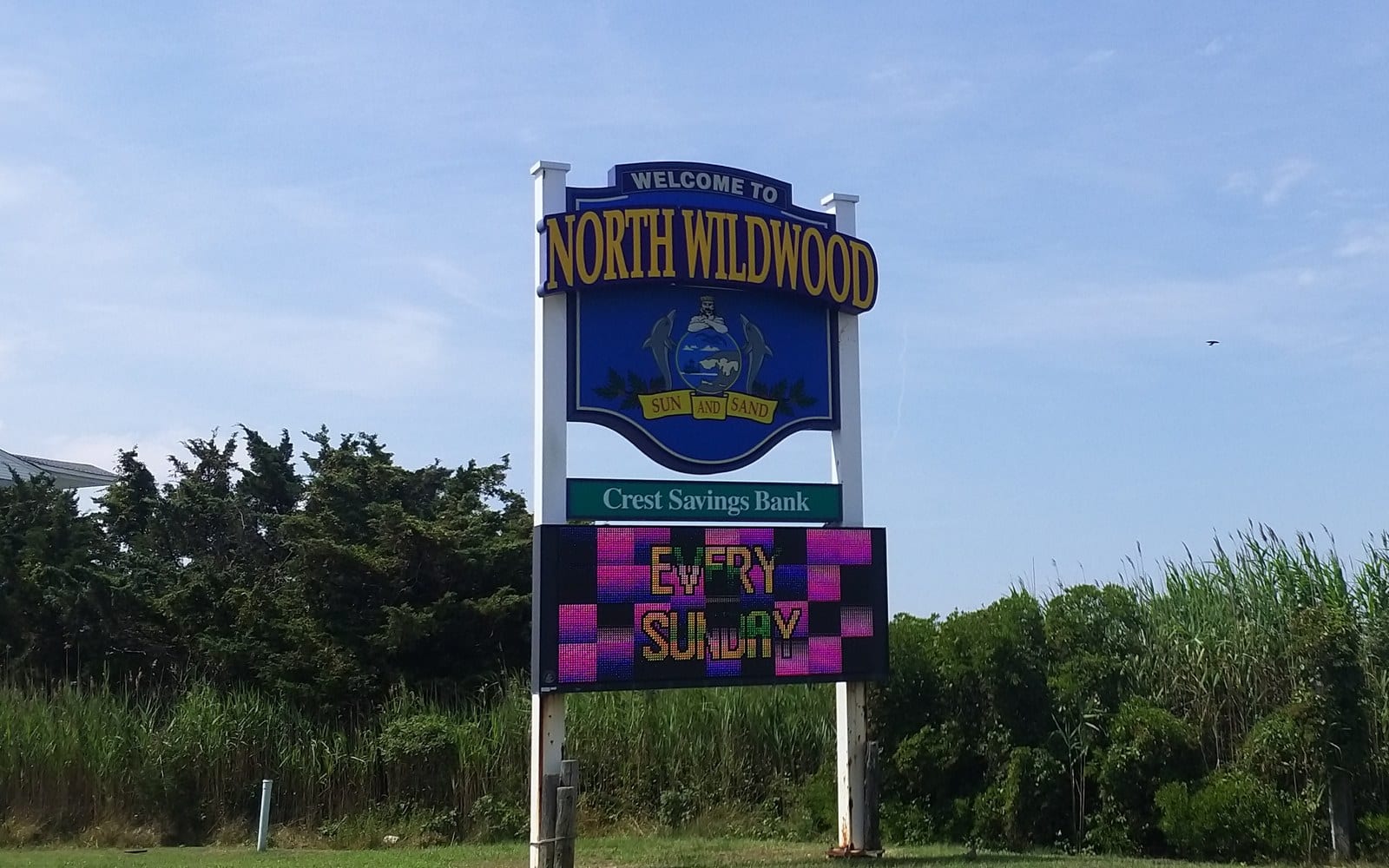 The Welcome to North Wildwood sign, with the city seal, beside a road lined with trees and tall grass